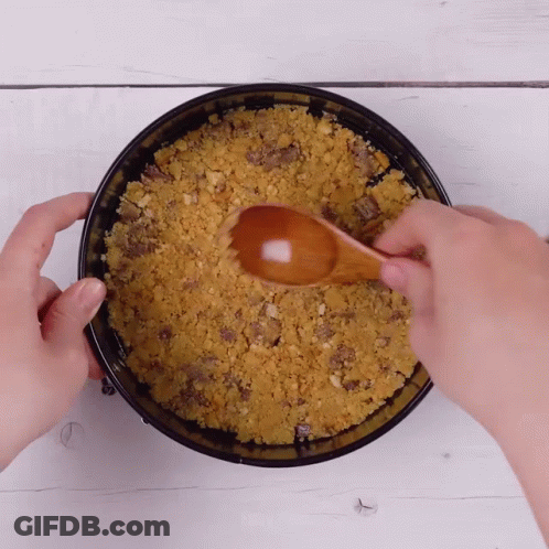 A Person Is Using A Wooden Spoon To Stir A Crumbly Crust In A Pan GIF