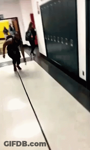 A Person Is Walking Down A Hallway With Lockers On The Wall . GIF