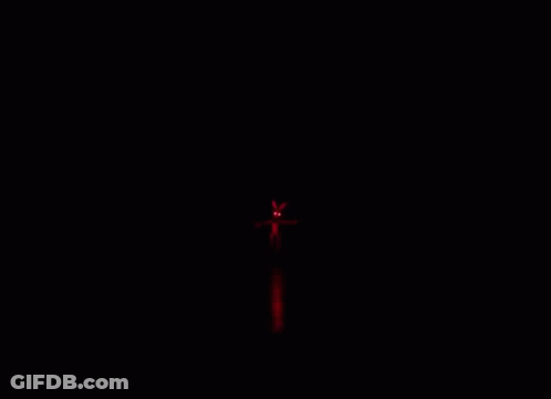A Person Is Walking Down A Hallway With Red Lights On The Ceiling . GIF