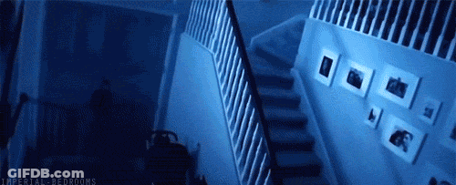 A Person Is Walking Down A Set Of Stairs In A Dark Room With Pictures On The Wall . GIF
