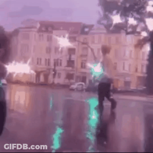 A Person Is Walking Down A Street In The Rain While Holding A Green Light . GIF