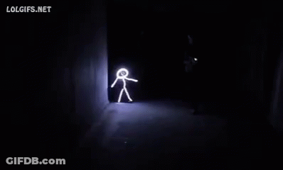 A Person Is Walking Through A Dark Room With A Stick Figure Drawn On The Wall . GIF