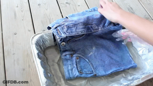 A Person Is Washing A Pair Of Jeans In A Tin Foil Tray GIF