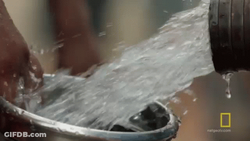 A Person Is Washing Their Hands In A Bucket Of Water From A Hose . GIF