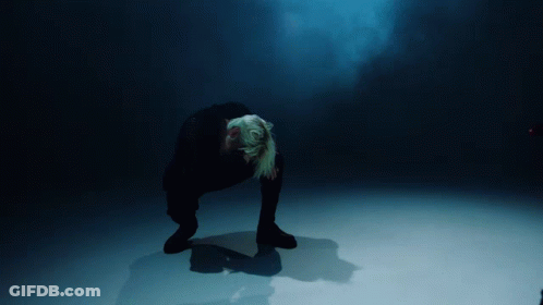A Person Kneeling Down In A Dark Room With A Blue Light Behind Them GIF