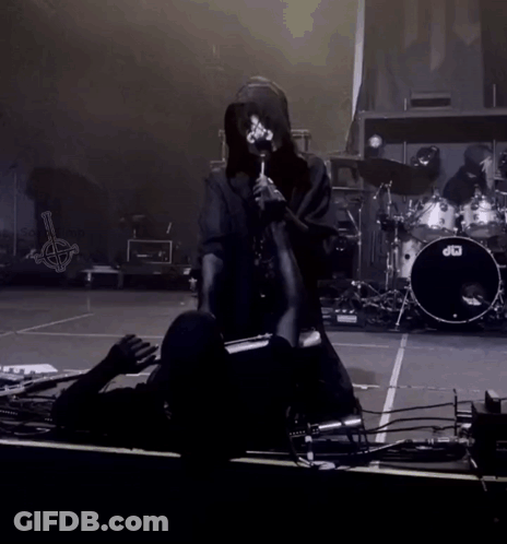 A Person Kneeling Down On A Stage With A Drum Set In The Background GIF