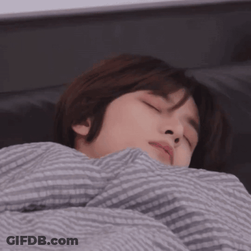 A Person Laying In Bed With Their Eyes Closed And A Striped Blanket GIF