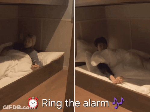 A Person Laying On A Bed Next To An Alarm Clock That Says " Ring The Alarm " On It GIF