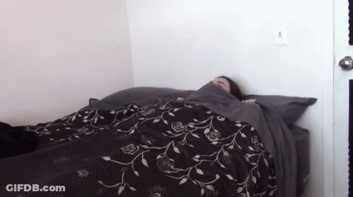 A Person Laying On A Bed With A Black And White Floral Blanket GIF