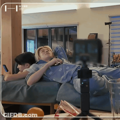 A Person Laying On A Bed With A Hybe Logo On The Corner GIF