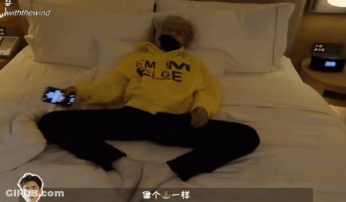 A Person Laying On A Bed With A Yellow Hoodie That Says Emm Alge GIF