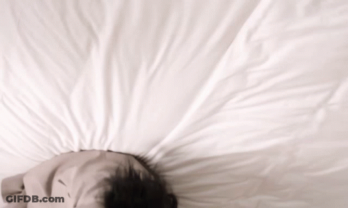 A Person Laying On A Bed With Their Head On A Pillow GIF