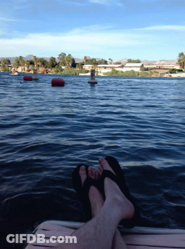 A Person Laying On A Dock With Their Feet In The Water With A Buoy In The Background GIF