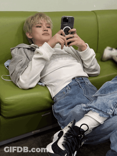 A Person Laying On A Green Couch Looking At Their Cell Phone GIF