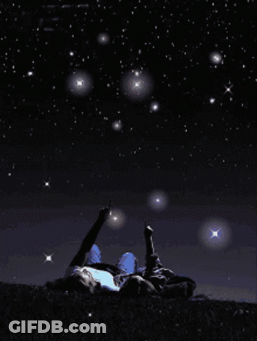 A Person Laying On The Ground Pointing At The Stars In The Night Sky GIF