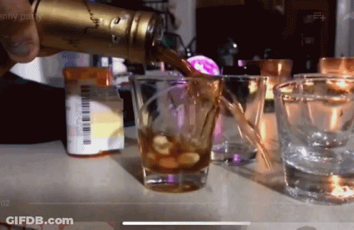 A Person Pouring A Drink Into A Shot Glass With A Pill Bottle In The Background GIF