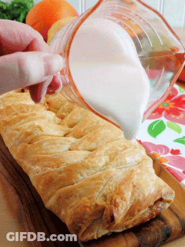 A Person Pouring Milk Into A Pastry On A Wooden Cutting Board GIF