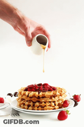 A Person Pouring Syrup Over A Stack Of Waffles With Strawberries On Top GIF