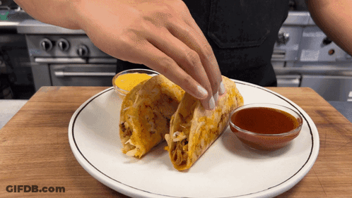 A Person Putting A Taco On A Plate With A Bowl Of Dipping Sauce GIF