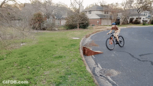 A Person Riding A Bike Down A Road With A Ramp GIF