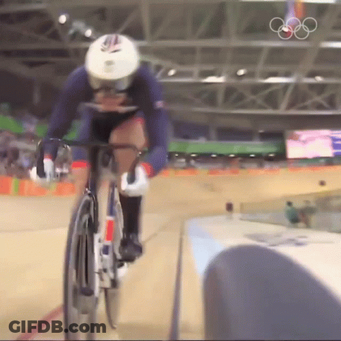 A Person Riding A Bike In A Stadium With The Olympic Rings In The Background GIF