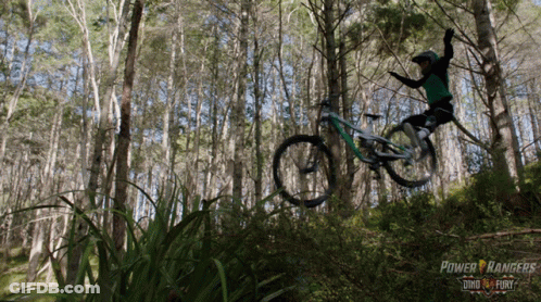 A Person Riding A Bike In The Woods With A Power Rangers Logo In The Background GIF