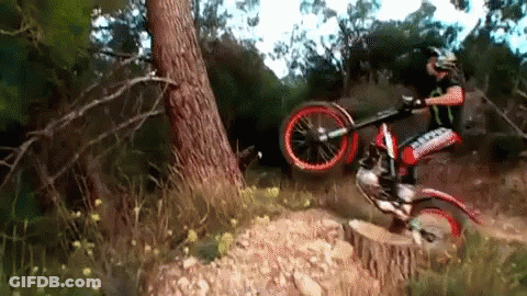 A Person Riding A Dirt Bike In The Woods With A Sticker On The Front That Says ' Simpson ' GIF