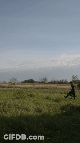 A Person Running In A Field With Trees In The Background GIF