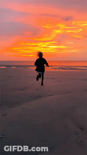 A Person Running On A Beach With A Sunset In The Background GIF