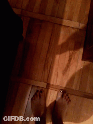 A Person 'S Feet Are Standing On A Wooden Floor In A Dark Room GIF