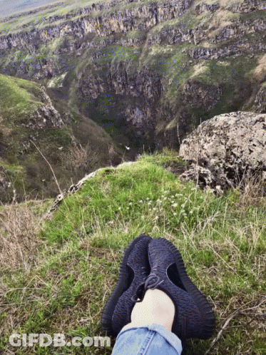 A Person 'S Feet Rest On A Grassy Hillside Overlooking A Valley GIF