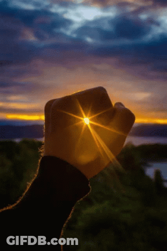 A Person 'S Fist Is Holding The Sun In Front Of A Sunset GIF