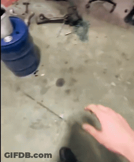 A Person 'S Hand Is Reaching For A Blue Barrel On A Dirty Floor GIF