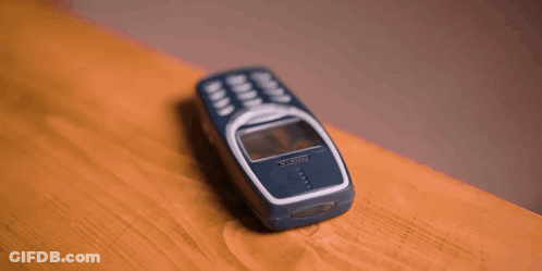 A Person 'S Hand Is Reaching For A Cell Phone On A Wooden Table . GIF
