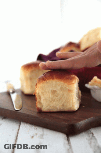 A Person 'S Hand Is Reaching For A Piece Of Bread On A Cutting Board GIF