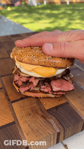 A Person 'S Hand Is Reaching For A Sandwich On A Cutting Board GIF