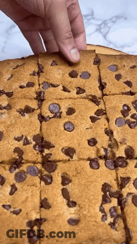 A Person 'S Hand Is Reaching Into A Cookie With Chocolate Chips GIF