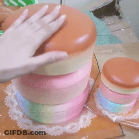 A Person 'S Hand Is Reaching Into A Stack Of Colorful Cakes On A Table GIF