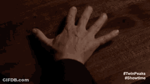 A Person 'S Hand Is Reaching Out Towards A Wooden Table . GIF