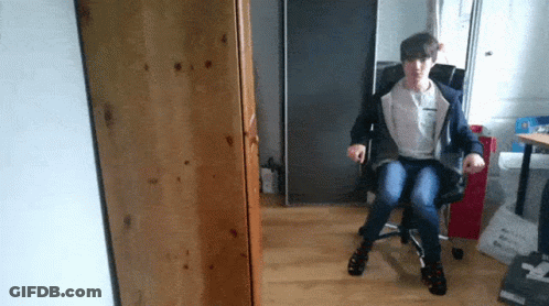 A Person Sitting In A Chair With The Letter T On The Back Of Their Shirt GIF