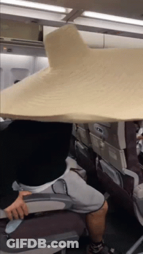 A Person Sitting On An Airplane With A Large Blanket Over Their Head GIF