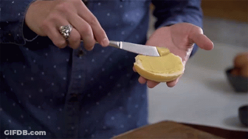 A Person Spreading Butter On A Slice Of Bread With A Knife GIF