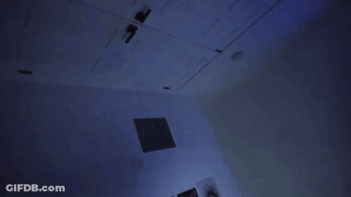 A Person Standing In A Dark Room With A Blue Light On The Wall GIF