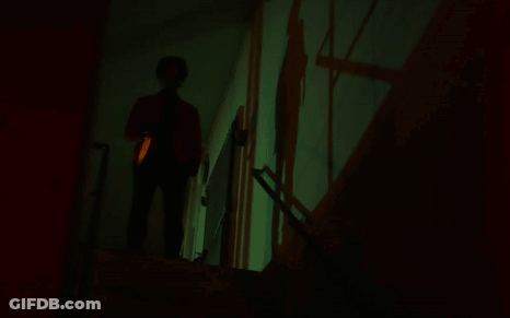 A Person Standing In A Dark Room With A Green Light Projected On The Wall GIF