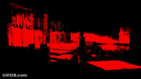 A Person Standing In A Dark Room With A Red Light Behind Them GIF