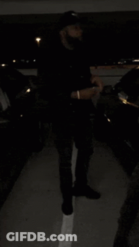 A Person Standing In A Parking Lot With Cars Parked In The Background GIF