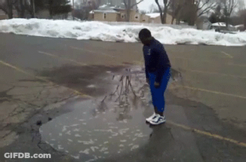 A Person Standing In A Puddle In A Parking Lot With Snow On The Ground GIF