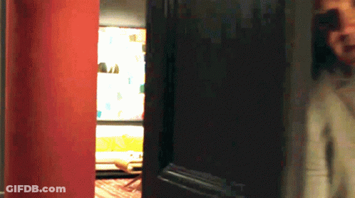 A Person Standing In Front Of A Door With A Red Wall Behind Them GIF