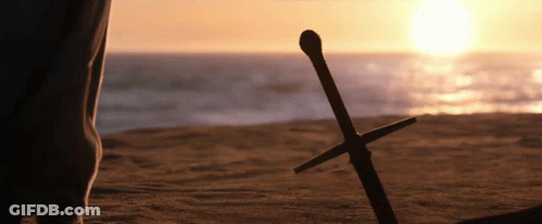 A Person Standing On A Beach With A Sword Laying On The Sand GIF