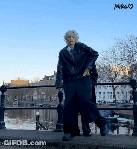 A Person Standing On A Bridge Next To A Body Of Water With The Word Mika Above Them GIF